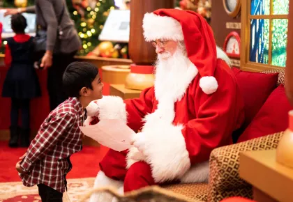 Kid slightly bowing to a seated Santa Claus
